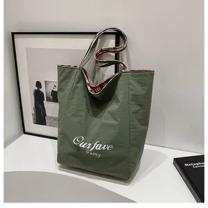 Detail of dark green canvas tote with white lettering and red checkered strap lining