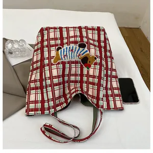 Close-up of red plaid canvas tote bag featuring cute cartoon dog embroidery and soft texture