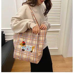 Detail of embroidered dachshund on checkered canvas tote bag worn by a model