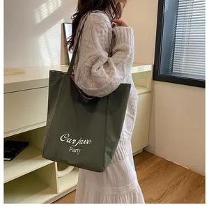 Olive green canvas tote bag with white lettering shown on shoulder for size reference