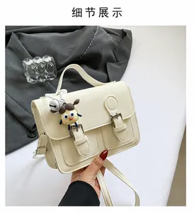 Detail of a vintage cream-colored crossbody bag with metal buckles and a cute charm