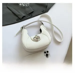Detail of white half-moon shoulder bag with silver flower buckle and smartphone for scale