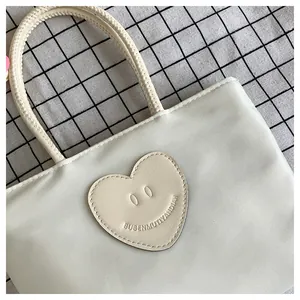 Dettaglio di una borsa in nylon crema con una toppa a forma di cuore e sorriso decorativo