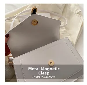 Close-up of golden hardware magnetic buckle on white minimalist flap crossbody bag