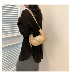 Detail of beige hobo shoulder bag featuring a silver flower buckle against a black shirt