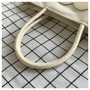 Dettaglio del manico della borsa in nylon crema con cuciture su panno a quadretti