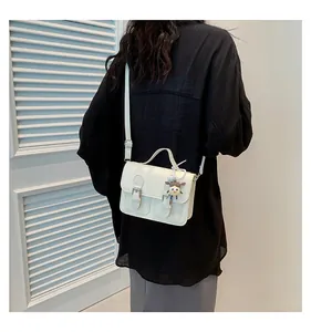 Detail of a white leather crossbody square bag with twin buckles and cute doll charm