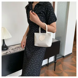 Dettaglio della borsa in nylon crema con patch a cuore e abito nero floreale