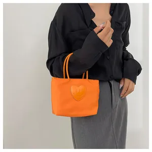 Detail of bright orange nylon tote bag with heart-shaped smiley face patch and dual handles