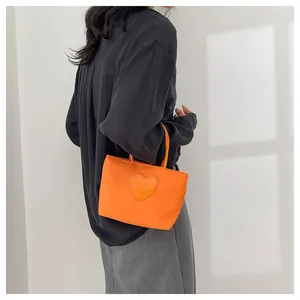 Dettaglio della mini borsa tote in nylon arancione con toppa cuore sorridente