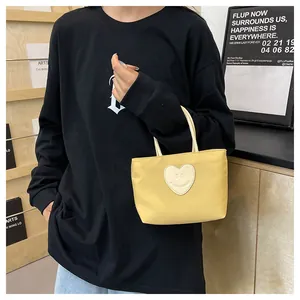Dettaglio della borsa tote in nylon giallo con toppa a cuore smiley bianca e manici
