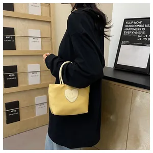 Dettaglio di una borsa gialla in nylon con patch a cuore sorridente su una modella