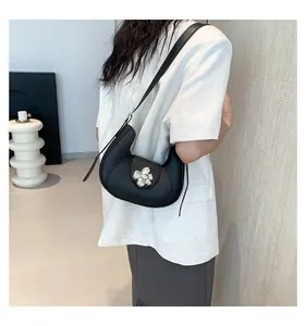 Detail of black crescent shoulder bag with silver floral buckle worn on white blazer