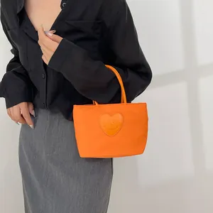 Mini borsa in nylon arancione vivace con patch a cuore sorridente su outfit scuro