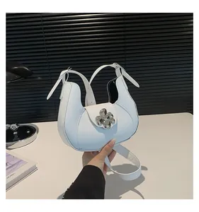 Close-up of white leather crescent bag with silver flower buckle and shoulder strap