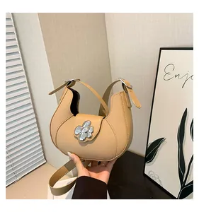 Close-up of beige underarm bag with a stylish silver flower buckle and semi-circular design