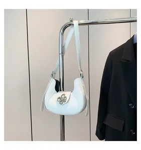 Detail of white leather hobo bag featuring a silver metal flower clasp and adjustable strap