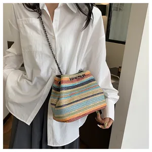 Détail d'un sac seau en paille tissée à rayures avec une bandoulière en chaîne