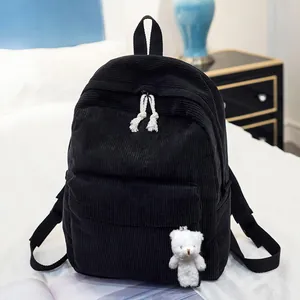 Detail of black corduroy backpack texture with plush bear charm in a cozy bedroom setting