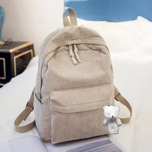 Detail view of a beige corduroy backpack with a plush bear charm in a cozy bedroom