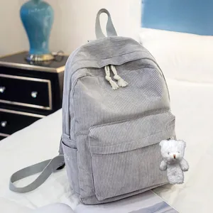 Detail of gray corduroy backpack with large front pocket and white bear pendant on a bed