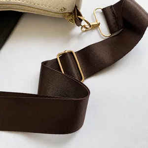 Detail of adjustable brown woven shoulder strap with gold metal buckle on white bag