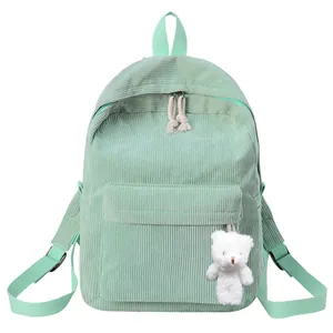 Close-up of mint green corduroy backpack with front pocket and plush bear pendant