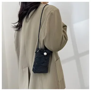 Dettaglio di una mini borsa a tracolla nera testurizzata con perla su un outfit blazer
