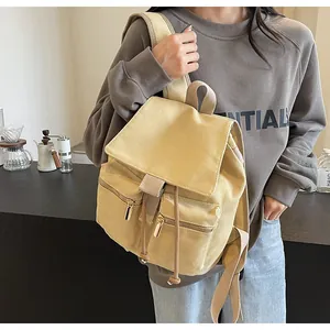 Detalle de mochila de lona beige con cordón y dos bolsillos frontales con cremallera dorada