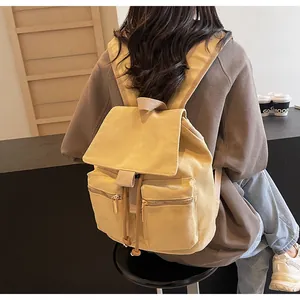 Detalle de mochila de lona amarillo claro con dos bolsillos frontales y cierre de cordón