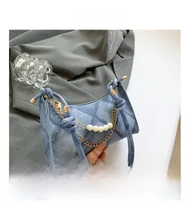 Détail du sac en denim bleu avec texture matelassée, chaînes d'or et perles blanches