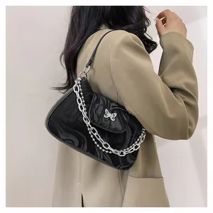 Detail of black patent leather shoulder bag with silver butterfly clasp and chain strap