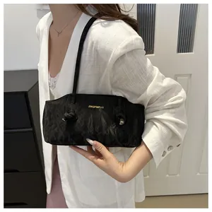Detail of a black textured underarm bag with gold logo lettering and a knotted shoulder strap