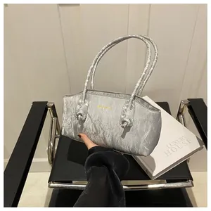 Detail of silver metallic textured underarm bag featuring a knotted handle and gold logo