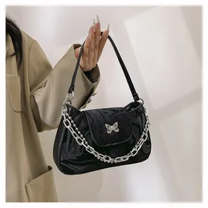 Detail of glossy black shoulder bag with silver butterfly charm and metal chain