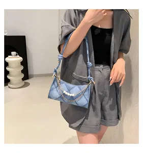 Détail du sac matelassé en jean bleu avec doubles chaînes en perles et métal doré avec nœud
