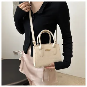 Detail of cream small square handbag with crocodile texture and gold metal plate on model