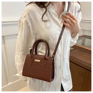 Close-up of a dark brown crocodile texture handbag with metallic plaque on white shirt