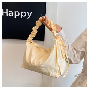 Detail der cremefarbenen Falten-Tasche mit Scrunchie-Griff und dekorativen Seitenbändern