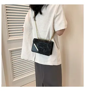 Detail of a black square shoulder bag with gold chain strap on a blazer outfit