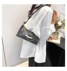 Détail du sac bandoulière matelassé noir avec chaîne dorée et perles blanches décoratives