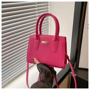 Detail of rose red croc-embossed handbag with gold metal plate and textured finish