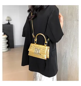 Detail der goldenen Krokodil-Handtasche mit Metallgriff und M-Logo an einem Modell