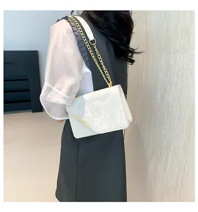 Detail view of white square bag featuring golden chain strap and subtle embossed texture