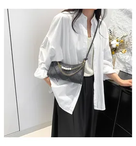 Sac en cuir matelassé noir avec chaînes dorées et perles sur une chemise blanche