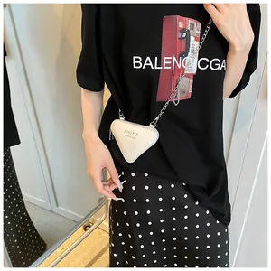 Détail d'un mini sac triangle blanc crème avec chaîne porté par un mannequin en scène
