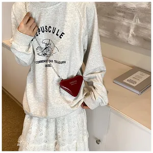 Détail d'un petit sac triangle rouge foncé porté avec une jupe en dentelle blanche