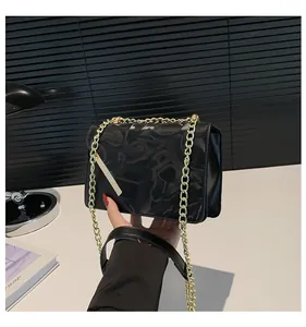 Detail view of black leather flap bag with gold chain and embossed monogram pattern