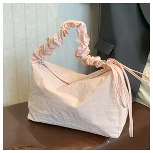 Detail der hellrosa gefalteten Handtasche mit Rüschen-Schultergurt auf einer Lederbank