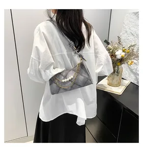 Détail d'un sac bandoulière gris matelassé avec perles et chaîne en métal doré